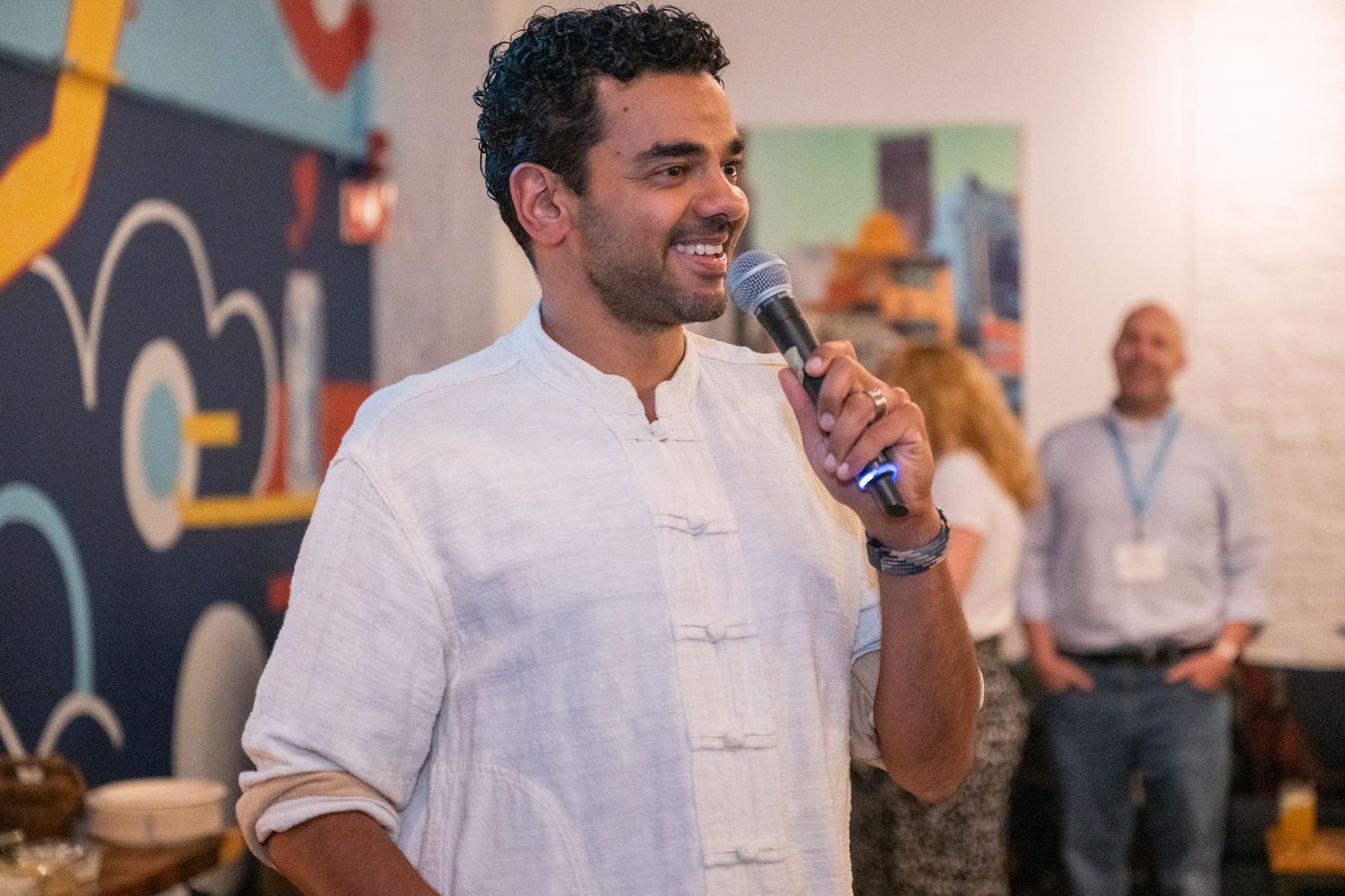 Gaurav Manchanda speaking with a microphone at a MassChallenge event with colorful illustrated wall in the background