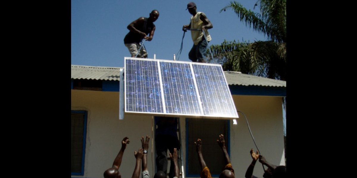 Solar panel installation on the roof of a Liberian health clinic with community members watching from below